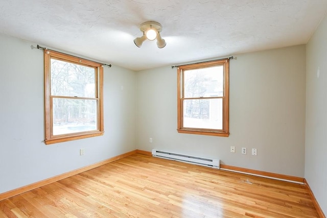 empty room with light wood-style floors, baseboard heating, baseboards, and a textured ceiling