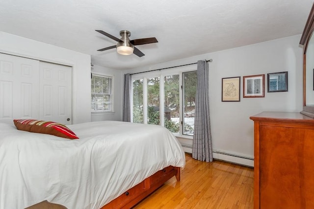 bedroom with light wood-type flooring, multiple windows, a baseboard heating unit, and a closet