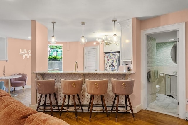 17 Gloucester St Unit A, Boston, MA 02115 - kitchen featuring freestanding refrigerator, light stone counters, white cabinetry, and a kitchen breakfast bar