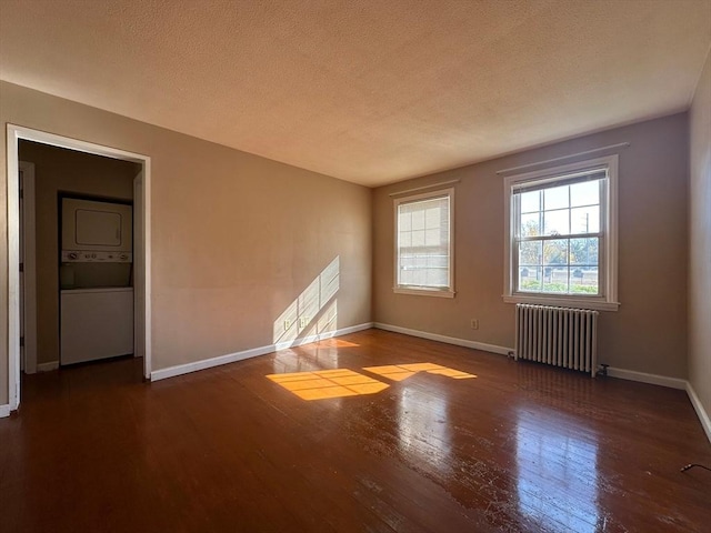 unfurnished room featuring dark wood-type flooring, radiator heating unit, stacked washer / dryer, and a textured ceiling