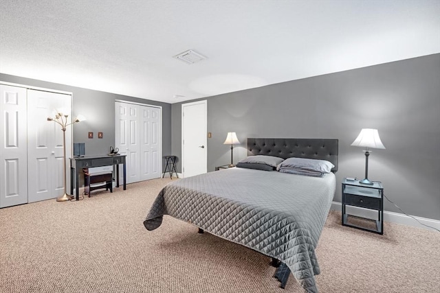 bedroom with visible vents, baseboards, two closets, and carpet flooring