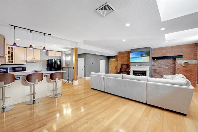 living area featuring visible vents, brick wall, light wood-type flooring, recessed lighting, and a skylight