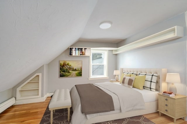 bedroom with vaulted ceiling, light wood-type flooring, and baseboard heating