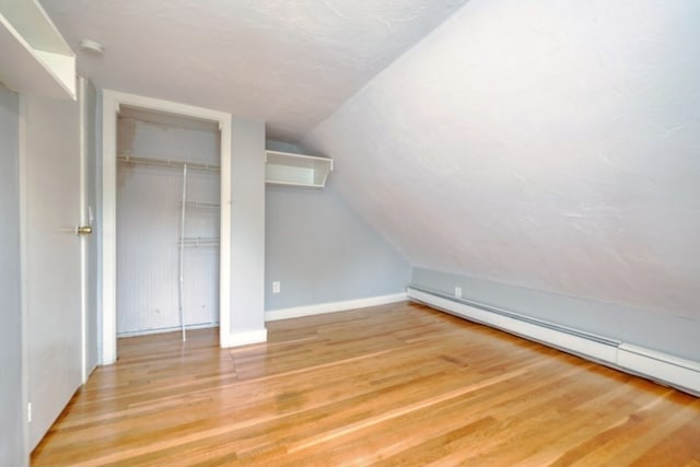 bonus room with a baseboard radiator, light wood-type flooring, and vaulted ceiling