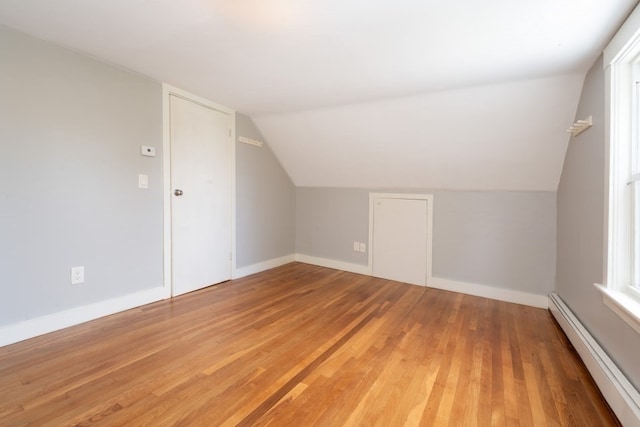 additional living space with vaulted ceiling, hardwood / wood-style floors, and a baseboard heating unit