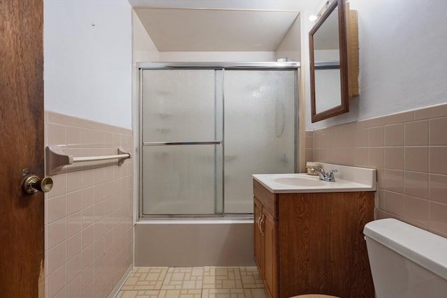 bathroom with a wainscoted wall, shower / bath combination with glass door, tile walls, toilet, and vanity