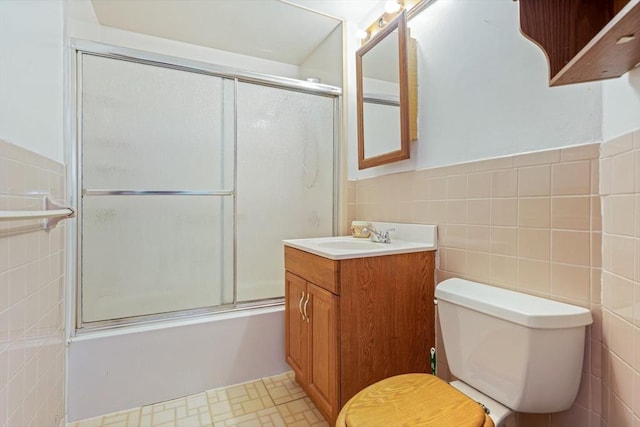 full bathroom with a wainscoted wall, shower / bath combination with glass door, tile walls, toilet, and vanity