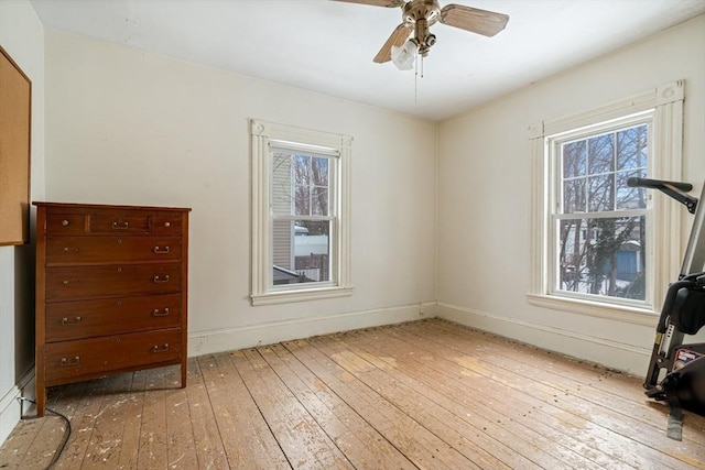 unfurnished bedroom featuring ceiling fan, multiple windows, wood finished floors, and baseboards