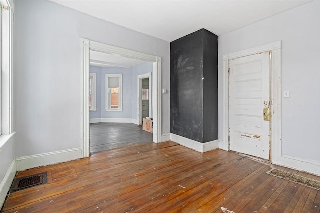 empty room with dark wood-type flooring, visible vents, and baseboards