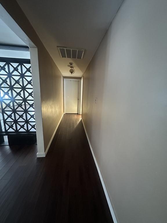 corridor with baseboards, visible vents, and dark wood finished floors