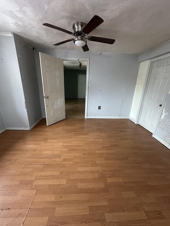 unfurnished bedroom featuring a textured ceiling, baseboards, and light wood-style floors