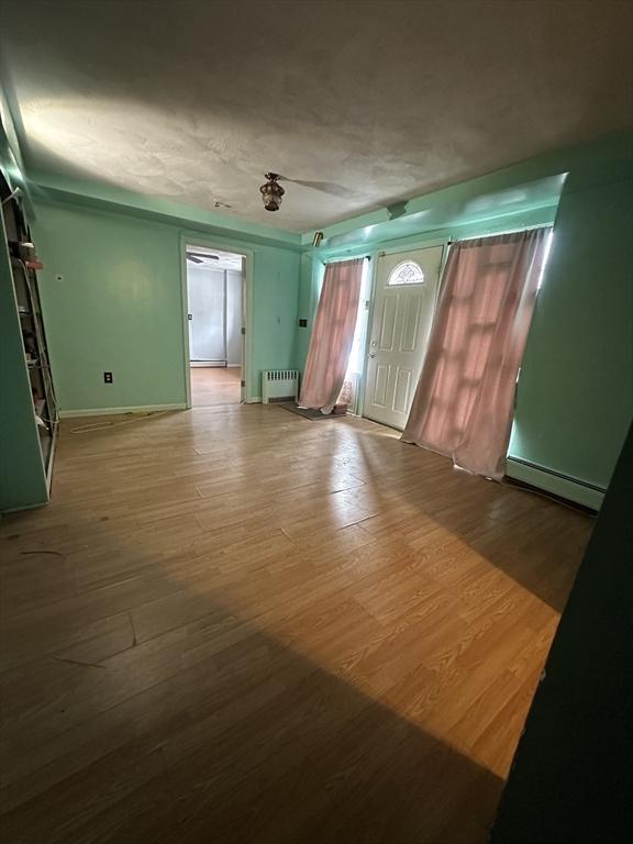 interior space with a baseboard heating unit, radiator, baseboards, and wood finished floors