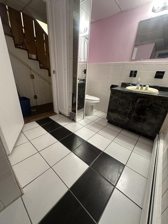 bathroom with tile walls, vanity, toilet, and tile patterned floors