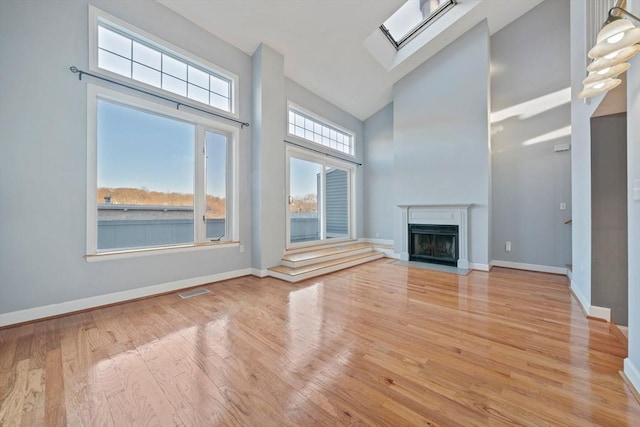 unfurnished living room featuring high vaulted ceiling, a skylight, and light hardwood / wood-style floors