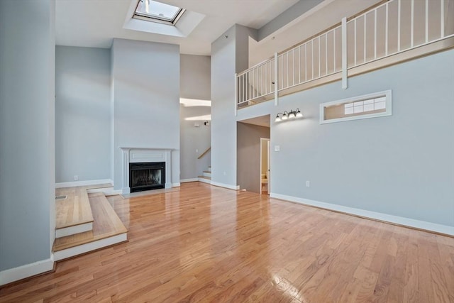 unfurnished living room with a towering ceiling, light hardwood / wood-style flooring, and a skylight