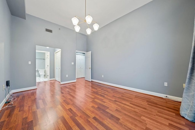 interior space featuring a notable chandelier, ensuite bath, wood-type flooring, and a high ceiling