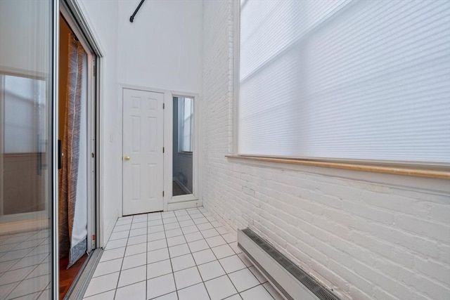 hallway featuring light tile patterned floors, a towering ceiling, and brick wall