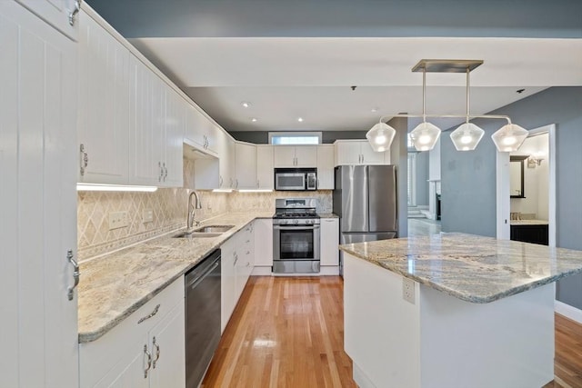 kitchen with stainless steel appliances, white cabinetry, sink, and decorative light fixtures