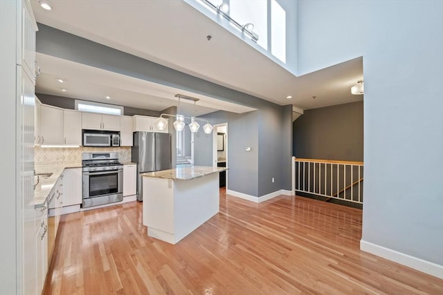 kitchen with appliances with stainless steel finishes, decorative light fixtures, white cabinets, a center island, and light wood-type flooring