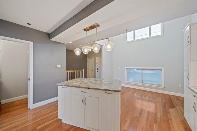 kitchen with light stone counters, a center island, hanging light fixtures, and white cabinets