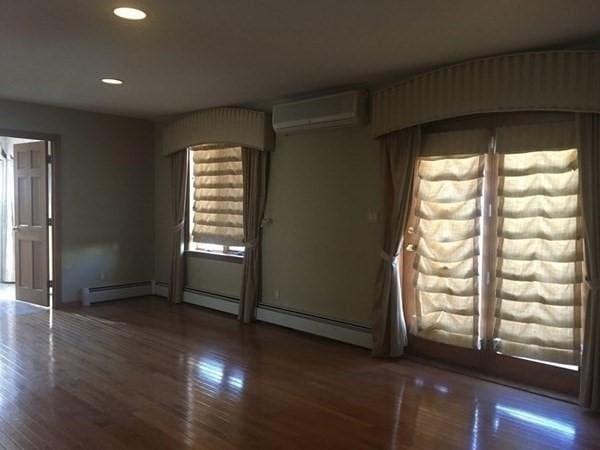 empty room featuring baseboard heating, a wall mounted AC, and dark hardwood / wood-style flooring