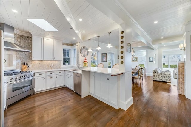 kitchen with kitchen peninsula, wall chimney exhaust hood, tasteful backsplash, white cabinetry, and stainless steel appliances