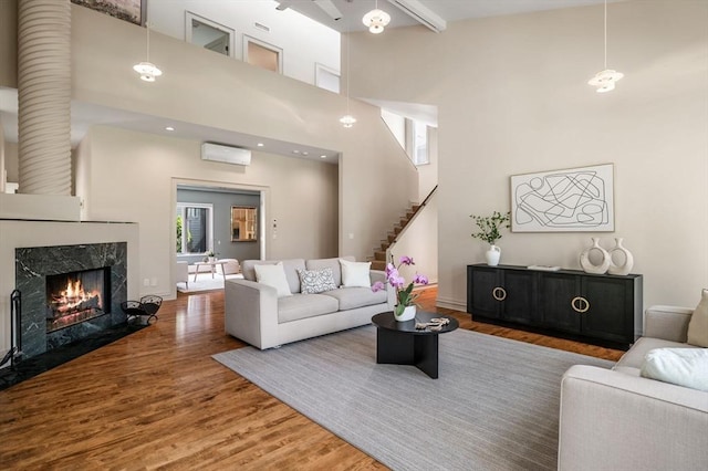 living area featuring an AC wall unit, wood finished floors, a premium fireplace, stairs, and a towering ceiling