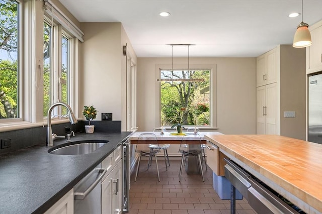 kitchen featuring a sink, stainless steel dishwasher, recessed lighting, pendant lighting, and dark tile patterned floors