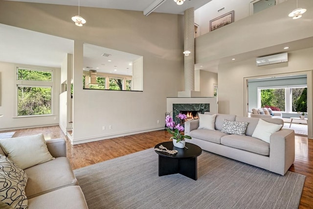 living room featuring a wall mounted air conditioner, wood finished floors, a high end fireplace, a towering ceiling, and baseboards
