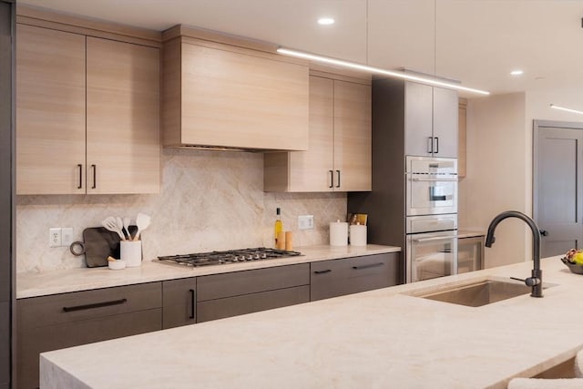 kitchen with white double oven, backsplash, premium range hood, sink, and stainless steel gas cooktop