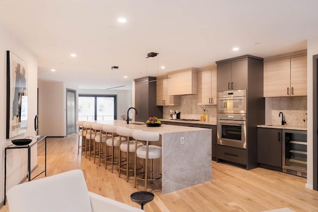 kitchen with stainless steel appliances, tasteful backsplash, wine cooler, light hardwood / wood-style flooring, and decorative light fixtures