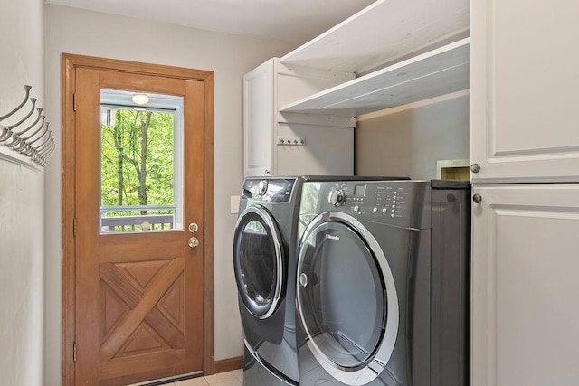 clothes washing area with washing machine and clothes dryer, cabinet space, light tile patterned flooring, and baseboards