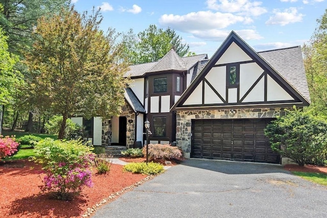 tudor house with stucco siding, stone siding, asphalt driveway, and roof with shingles