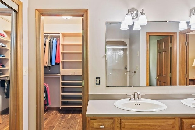 bathroom with a walk in closet, double vanity, and wood finished floors