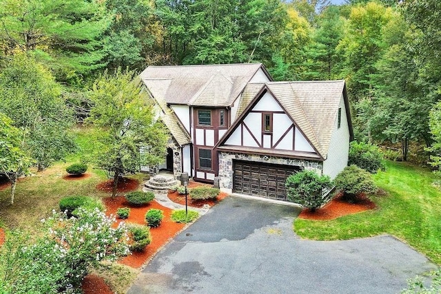 tudor house featuring driveway, stucco siding, a wooded view, and stone siding