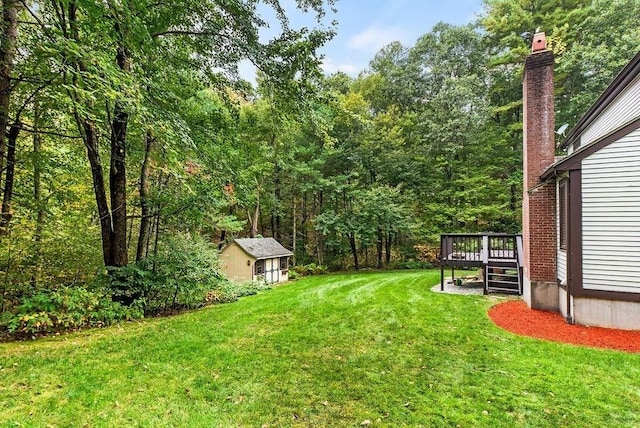 view of green lawn with a wooden deck, a shed, an outbuilding, and a view of trees