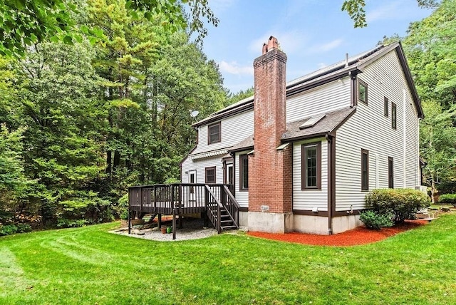 back of house with a wooden deck, a chimney, and a lawn