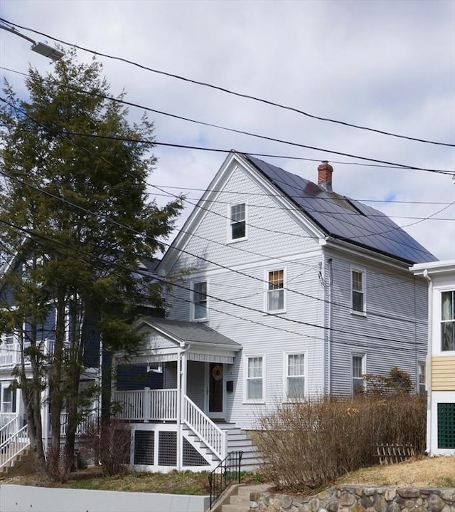 view of front of property featuring roof mounted solar panels, a chimney, and covered porch
