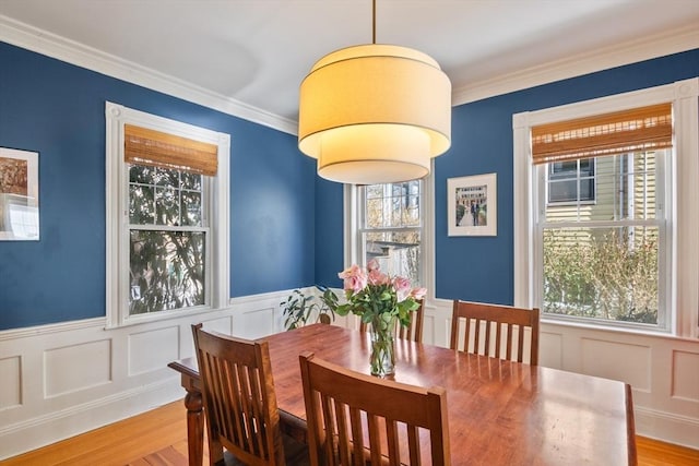 dining space with wood finished floors, a wainscoted wall, crown molding, and a decorative wall