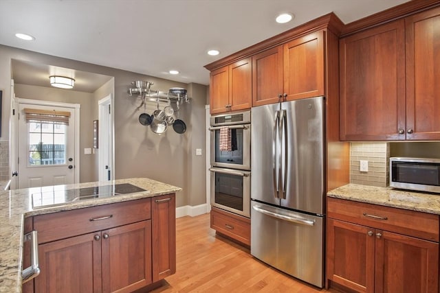 kitchen featuring appliances with stainless steel finishes, light wood finished floors, decorative backsplash, brown cabinetry, and light stone countertops