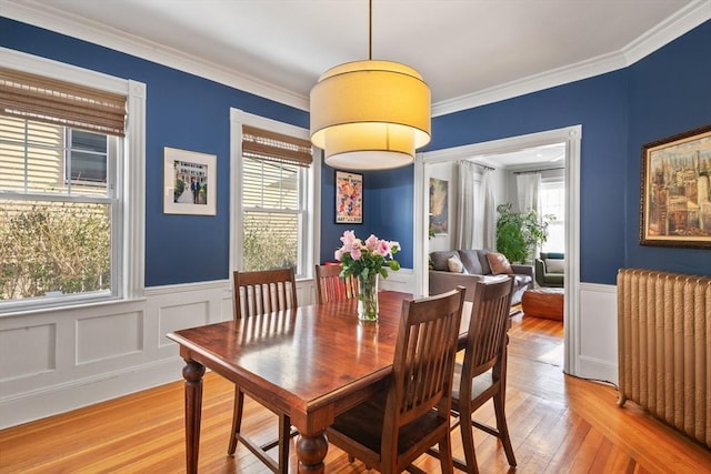 dining area with radiator, light wood-type flooring, healthy amount of natural light, a wainscoted wall, and crown molding