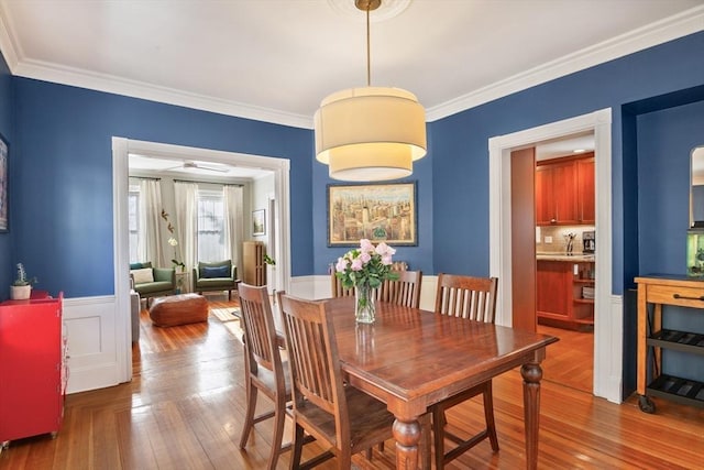 dining area with hardwood / wood-style floors, ornamental molding, and a wainscoted wall