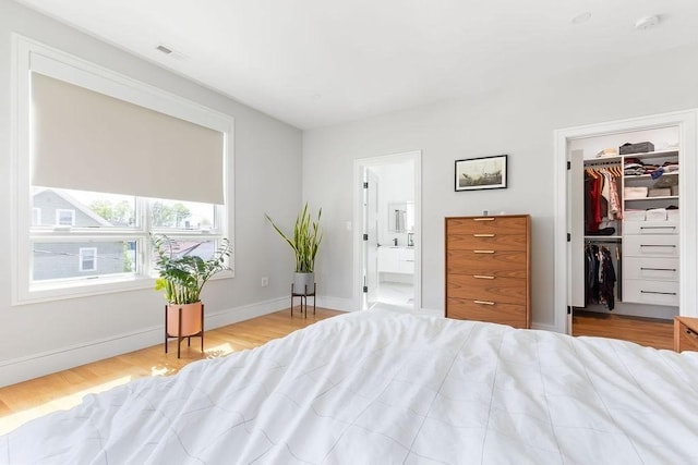 bedroom featuring visible vents, wood finished floors, baseboards, connected bathroom, and a spacious closet