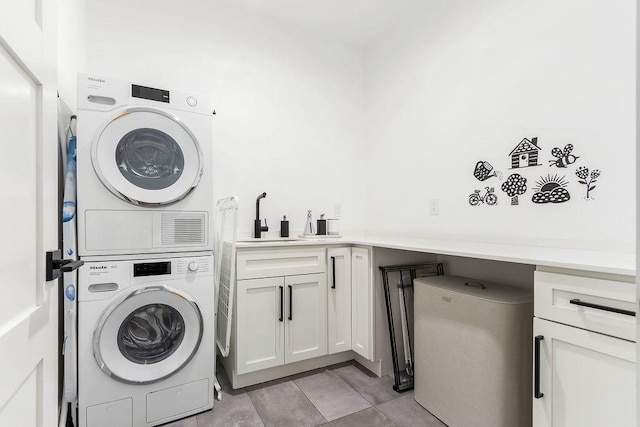 laundry area featuring cabinet space, light tile patterned floors, stacked washer / drying machine, and a sink