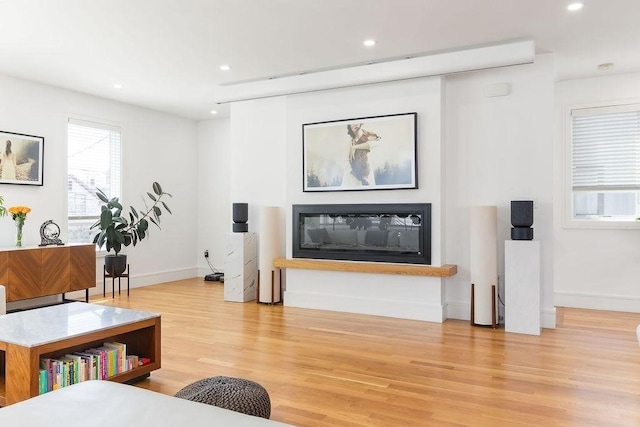 living room with recessed lighting, baseboards, a glass covered fireplace, and light wood finished floors