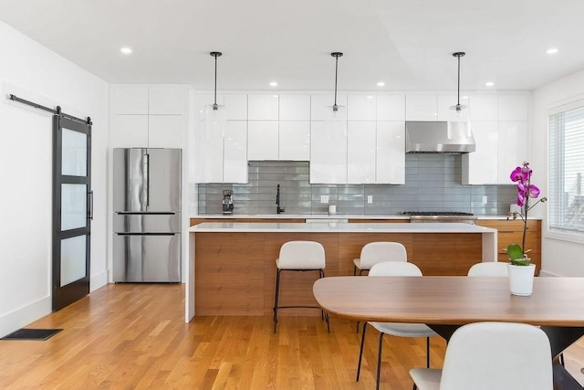 kitchen featuring exhaust hood, appliances with stainless steel finishes, a barn door, a kitchen island, and modern cabinets