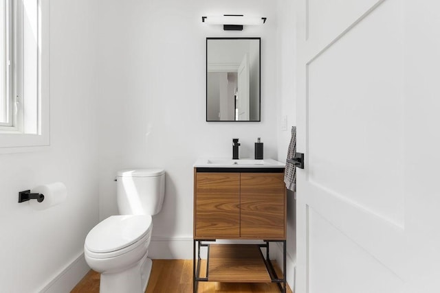 half bath featuring vanity, baseboards, toilet, and wood finished floors
