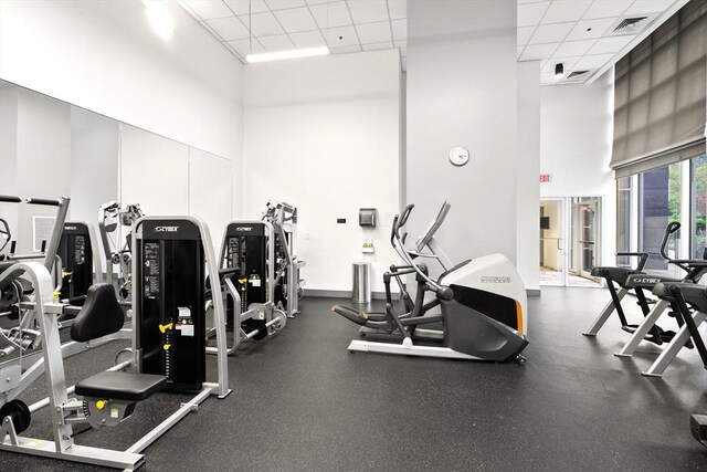 exercise room featuring a high ceiling, a paneled ceiling, and baseboards