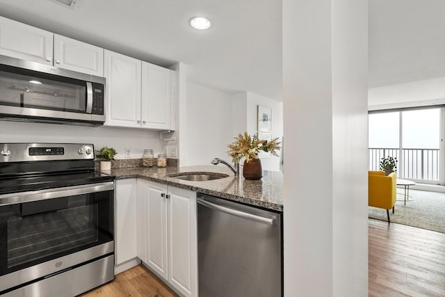 kitchen with stainless steel appliances, a sink, dark stone counters, light wood finished floors, and white cabinets