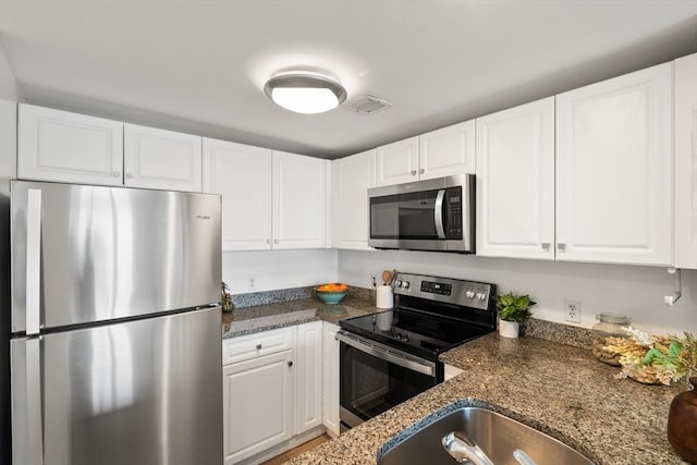kitchen with stainless steel appliances, white cabinetry, and dark stone counters